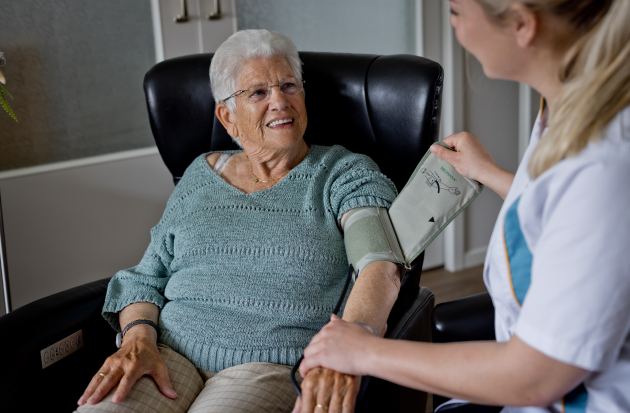 Wijkverpleegkundige meet de bloeddruk bij dame in thuiszorg 