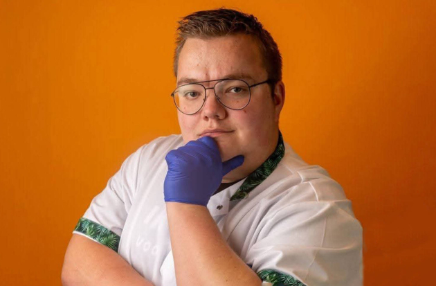 Coördinerend verzorgende Roy Korbijn staat met witte jas vastberaden op de foto. Zijn gehandschoende hand ondersteund zijn kin.