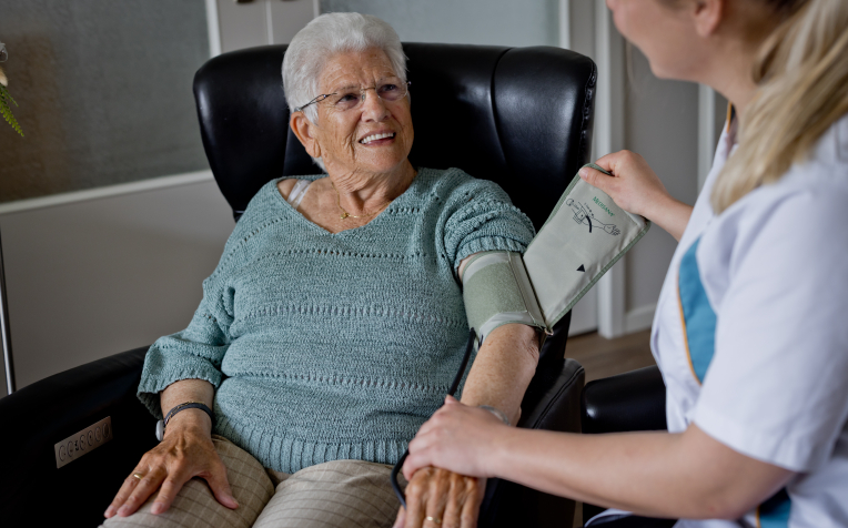 Wijkverpleegkundige meet de bloeddruk bij dame in thuiszorg 