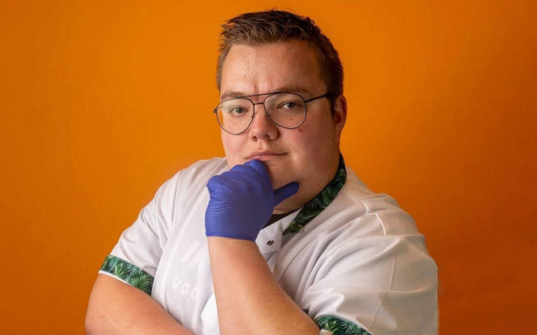 Coördinerend verzorgende Roy Korbijn staat met witte jas vastberaden op de foto. Zijn gehandschoende hand ondersteund zijn kin.