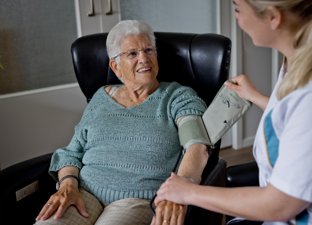 Wijkverpleegkundige meet de bloeddruk bij dame in thuiszorg 