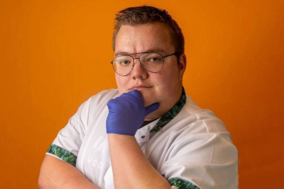 Coördinerend verzorgende Roy Korbijn staat met witte jas vastberaden op de foto. Zijn gehandschoende hand ondersteund zijn kin.